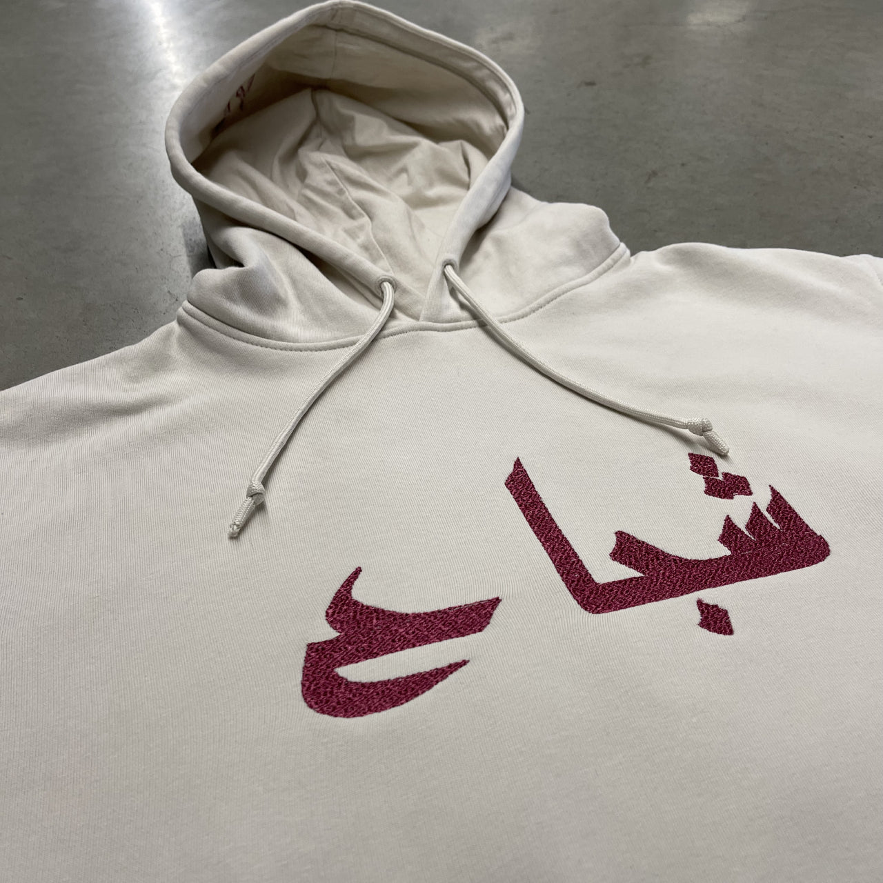 sweat à capuche blanc cassé et broderie rouge écriture arabe